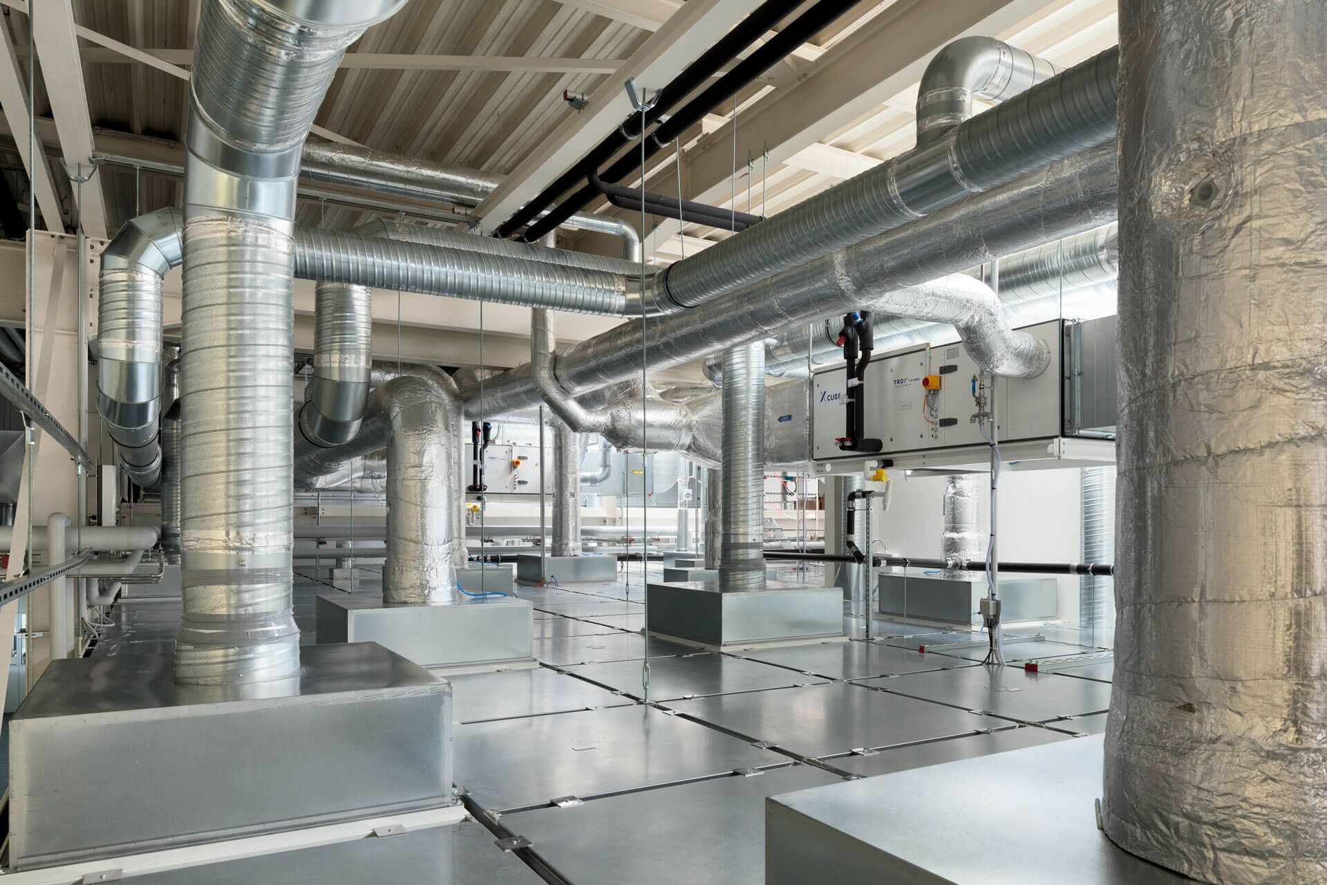 Ein moderner Industrieraum voller Metallkanäle und Belüftungssysteme, die ein komplexes Netzwerk über den Köpfen und entlang des Bodens darstellen.