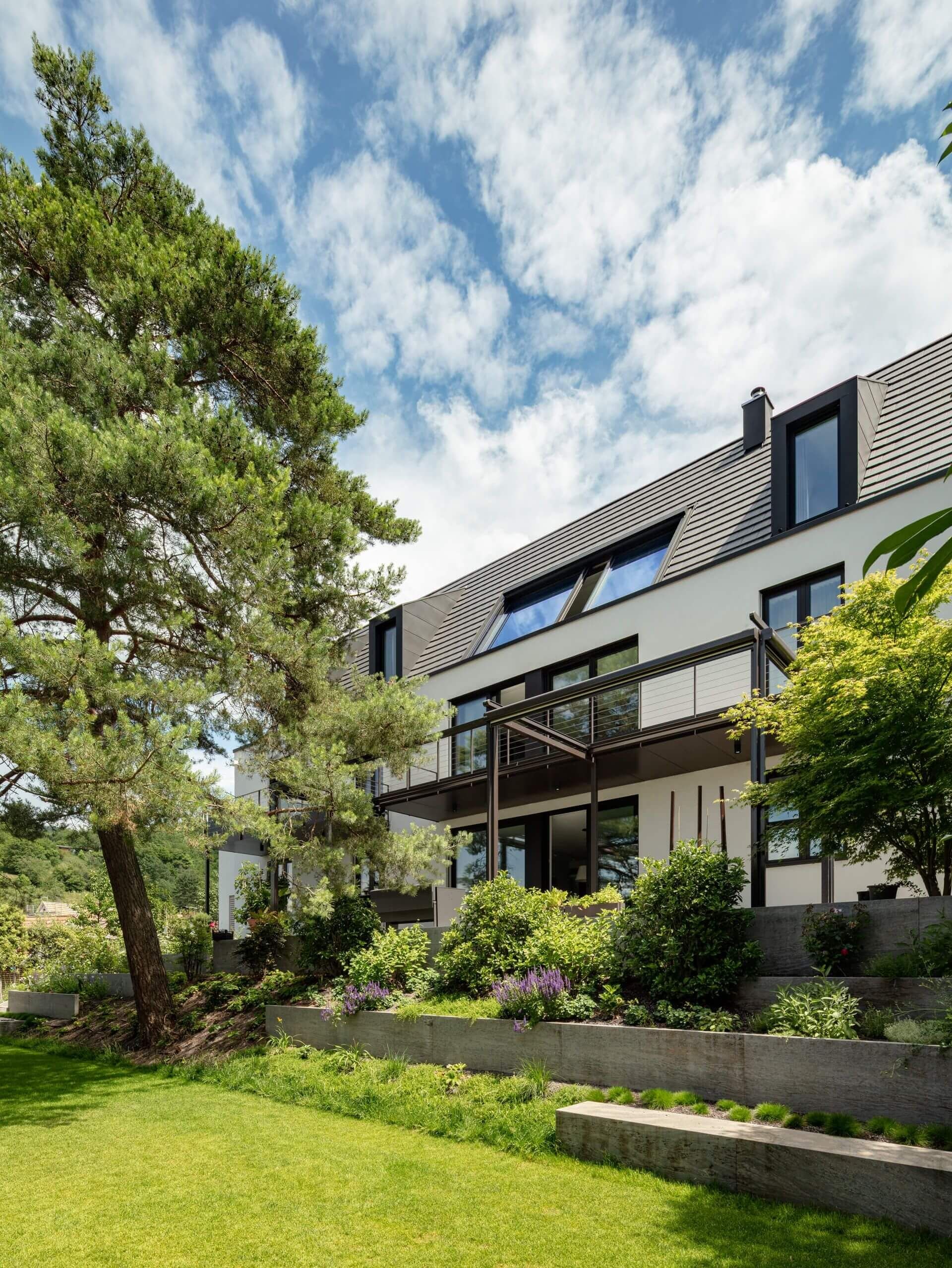 Modernes Haus mit elegantem Design, umgeben von üppigem Grün und einem blauen Himmel mit vereinzelten Wolken.