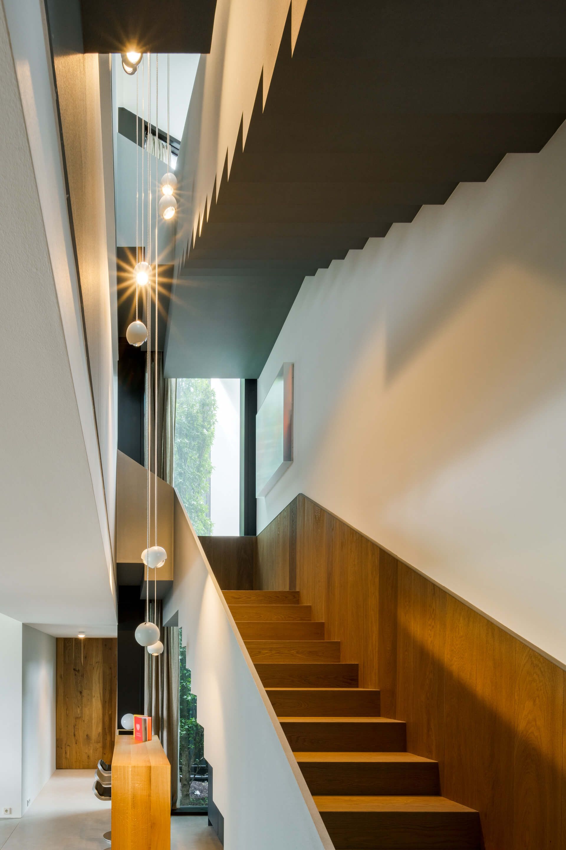 Moderne Treppe mit Holzstufen, eleganten weißen Wänden und stilvollen Pendelleuchten, die ein minimalistisches architektonisches Design zur Geltung bringen.